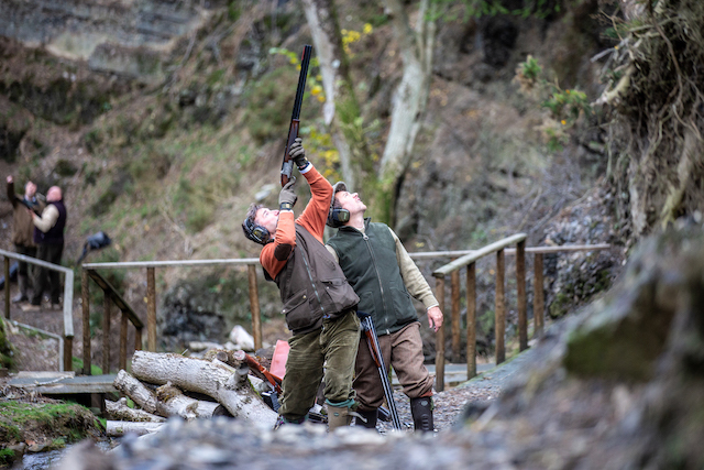 two men stood next to each other, one is pointing a gun up at the sky