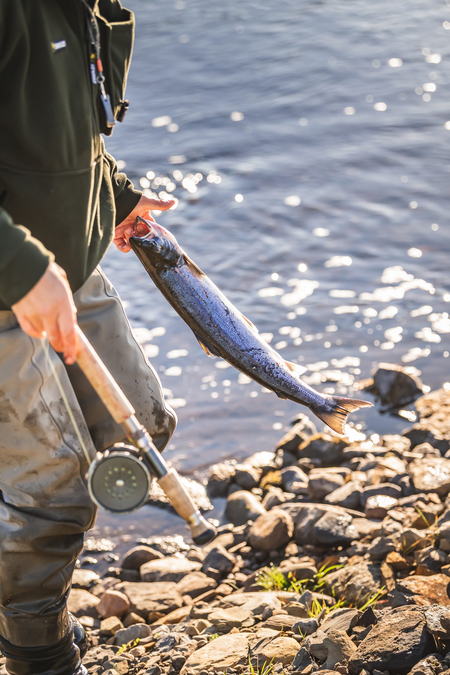 A man holding a reel and a salmon in his hand