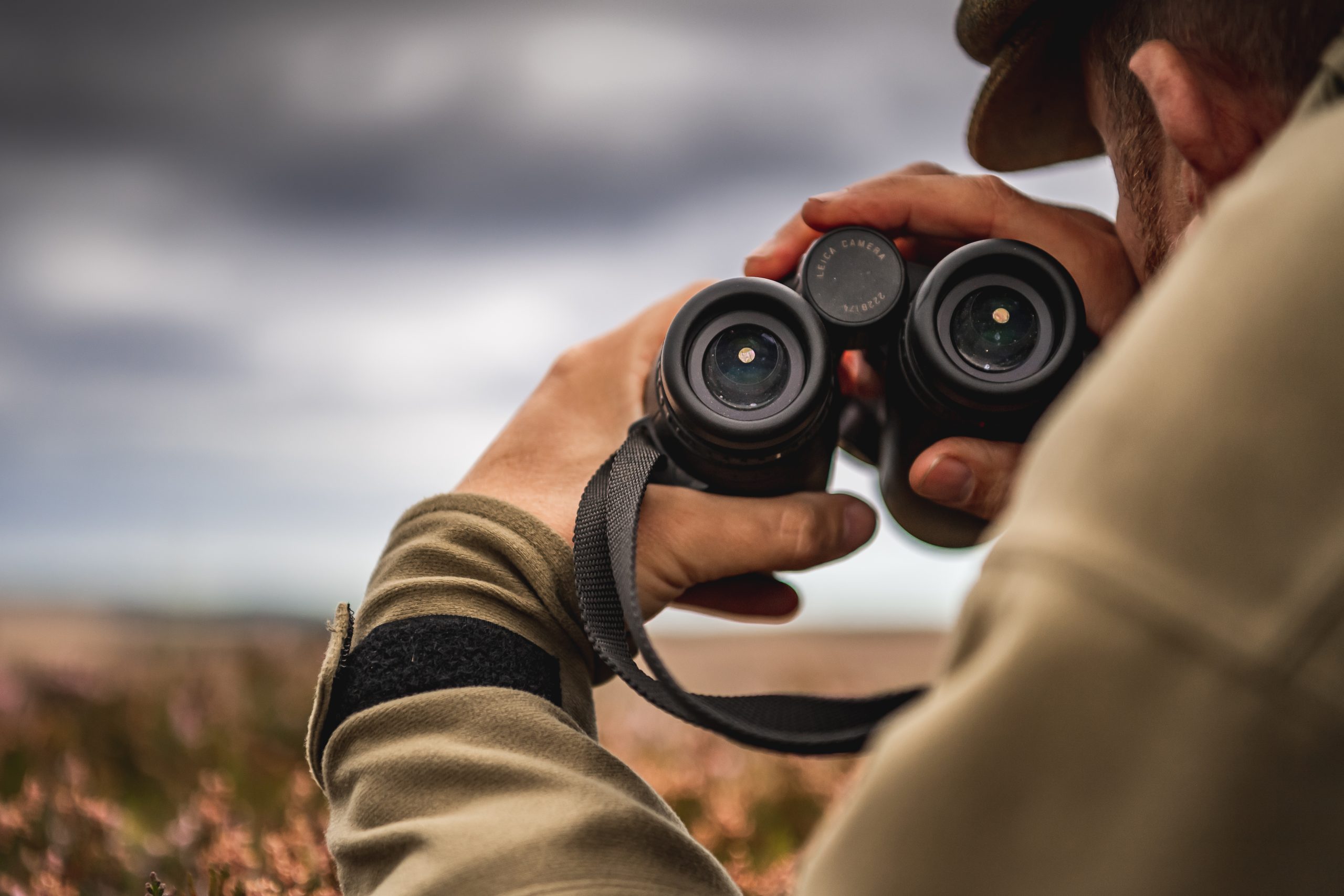 A set of binoculars being help by a man laying on heather