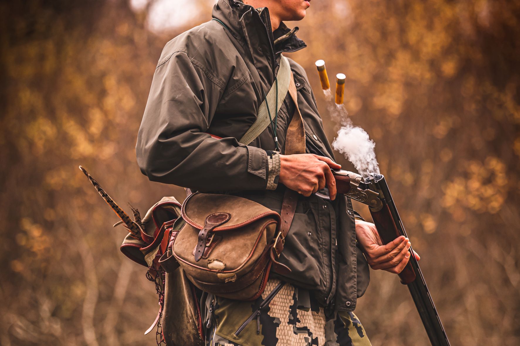 image of man from shoulders down holding onto shotgun, the cartridge has popped out and is smoking