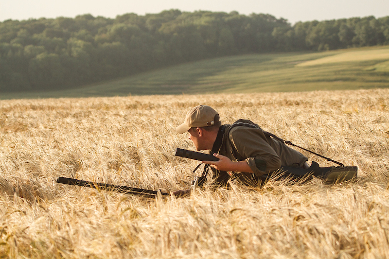 man crouched low stalking deer in a golden wheat field